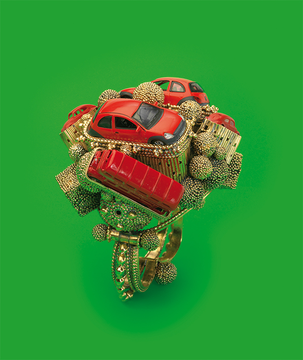 A sculpture of gold-tone pieces and red toy cars and buses, against a green background.